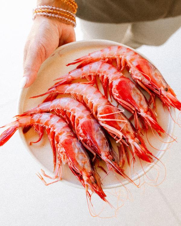 Unas manos sostienen un plato de gambas rojas del Mediterráneo